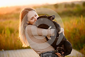 Woman holds in her arms, kisses a dog, looks at him lovingly,at sunset.The concept of friendship,trust,love, childfree