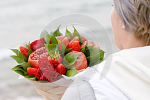 Woman holds in her hands a beautiful bouquet of apples, pomegranate, strawberries and flowers