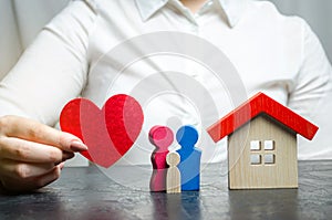 A woman holds in her hands a red heart near a miniature family and home. The concept of property insurance and house. Home