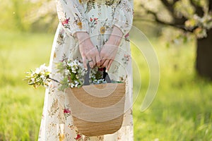 A woman holds in her hands a stylish wicker bag with blooming flowers in green park. Spring romantic mood and beuaty of nature photo