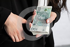 The woman holds her right hand in her pocket and squeezes a thick bundle of banknotes in her left