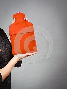 Woman holds hot water bottle in red fleece cover