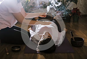 Woman holds incense over  man lying on  yoga mat. Esoteric massage concept