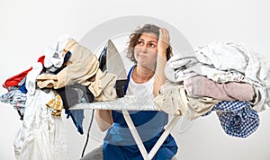 A woman holds an iron in her hands and sits at the ironing table. dirty laundry before ironing after washing