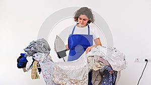 A woman holds an iron in her hands and sits at the ironing table. dirty laundry before ironing after washing. home