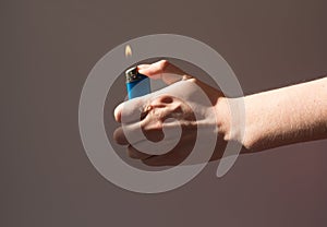 A woman holds a lighter with burning fire in the shade. Hands that are lighter on the gray background