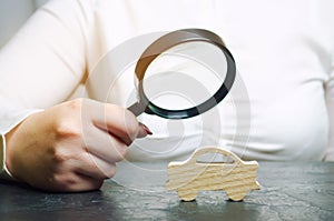 A woman holds a magnifying glass over a miniature wooden car. The estimated cost of the auto. Analysis and technical inspection of