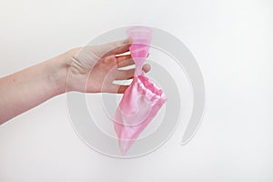 A woman holds a menstrual cup in her hand on a pink background. The concept of women`s health, hygiene, alternatives pads and photo