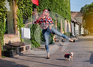 Fashionably dressed girl at the window of a boutique selling clothes. A woman holds a mini chihuahua in her arms. The pet is