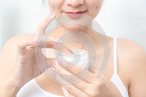 A woman holds a moisturizer in her hand and her skin and wrinkle from impurities