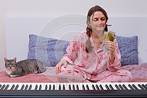 A woman holds money in euros next to a piano. Cat and woman sitting on a bed in a home bedroom