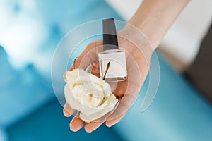 Woman holds nail varnish and a flower, beauty salon