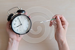 Woman holds a negative pregnancy test and alarm clock. Female fertility biological clock concept. One strip.