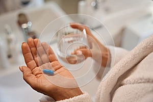 Woman holds painkiller pill and glass of water in her hand