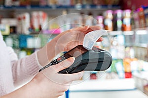 A woman holds a payment terminal while holding a receipt for completing a purchase. Hands close up and side view. The concept of