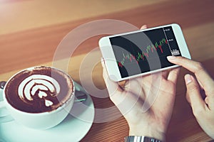 The woman holds the phone on a table with a graphical screen to invest the stock`s value. Investment concepts that rely on decisi