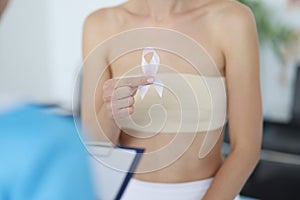 Woman holds pink ribbon in her hand during breast examination at doctor appointment