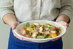 A woman holds a plate with a panzanella salad in her hands. Rustic style.