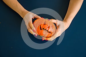 Woman holds pumpkin with cut out face for halloween lamp on black table. Close-up of female hands making jack-o`-lantern on the