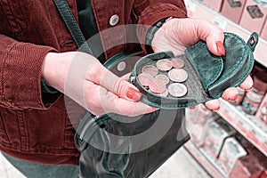 A woman holds a purse with several coins in her hand. After paying for purchases in the store, check in hand.