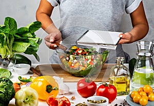 Woman holds recipe book with place for text in her hand and cooking healthy food in the kitchen. Healthy vegan food