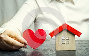 A woman holds a red heart near the wooden house. Insurance agent services. Property insurance concept. Protection of housing.