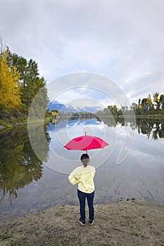 Woman holds red umbrella by calm river