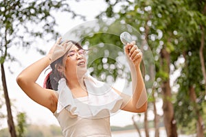 A woman holds a small fan and wipes her sweat on her face while walking outdoors on a hot day