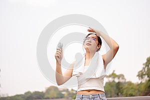 A woman holds a small fan and wipes her sweat on her face while walking outdoors on a hot day