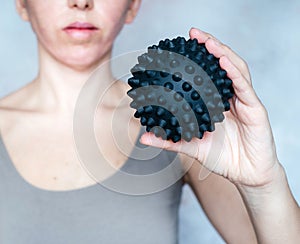 A woman holds a spiky trigger point massage ball used for muscle pain treatment and deep tissue massage