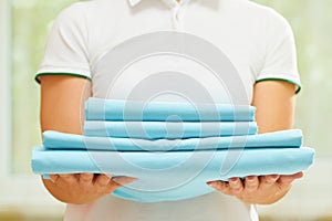 A woman holds a stack of clean folded blue bedding. Blurred background. Close-up