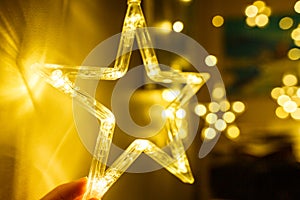 Woman holds Stylish christmas golden star illumination with gold baubles, golden lights bokeh at home interior. Christmas decor.