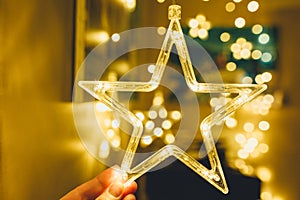 Woman holds Stylish christmas golden star illumination with gold baubles, golden lights bokeh at home interior. Christmas decor.