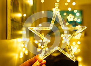 Woman holds Stylish christmas golden star illumination with gold baubles, golden lights bokeh at home interior. Christmas decor.