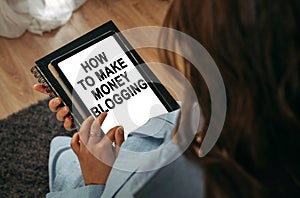 A woman holds a tablet in her hands on the screen of which it is written - How To Make Money Blogging