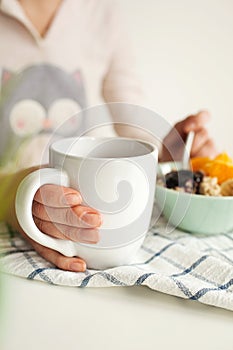 Woman holds tea cup and spoon with porridge and fruits