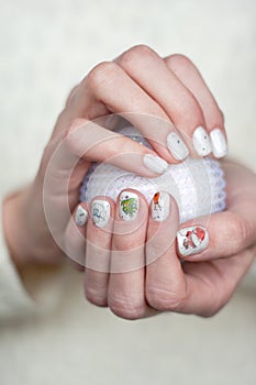 A woman holds a white Christmas ball in her palms. Festive New Year`s manicure. Female hands