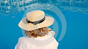 woman holds a white cup of coffee in her hands on the background of a blue swimming pool. Good morning enjoyment concept