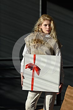 A woman holds a white gift box with a red ribbon