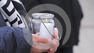 A woman holds a white large church candle in a glass candle holder outside in the cold season