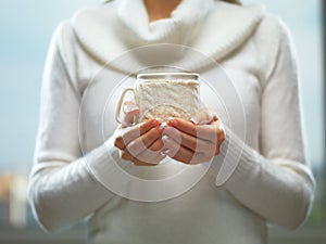 Woman holds a winter cup close up. Woman hands with elegant french manicure nails design holding a cozy knitted mug.