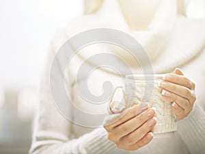 Woman holds a winter cup close up. Woman hands with elegant french manicure nails design holding cozy knitted mug.