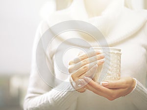 Woman holds a winter cup close up. Woman hands with elegant french manicure nails design holding a cozy knitted mug.