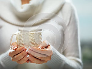 Woman holds a winter cup close up. Woman hands with elegant french manicure nails design holding a cozy knitted mug.