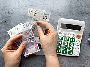 a woman holds zloty money and calculates expenses with a calculator. Financial concept