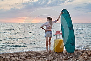 Woman on holiday, surfboard and suitcase. Sunset over ocean, sense of adventure and relaxation time concept. Copy space