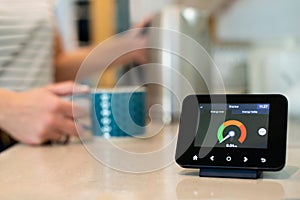 Woman At Home Boiling Kettle For Hot Drink With Smart Energy Meter In Foreground