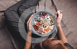 Woman in home clothes eating vegan Rice coconut porridge with figs, berries, nuts. Healthy breakfast ingredients