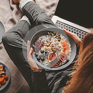 Woman in home clothes eating vegan Rice coconut porridge with figs, berries, nuts. Healthy breakfast ingredients.