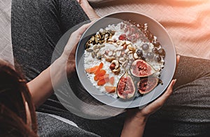 Woman in home clothes eating vegan Rice coconut porridge with figs, berries, nuts. Healthy breakfast ingredients